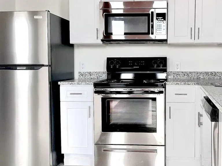 Stainless steel kitchen appliances: refrigerator, microwave, oven, white cabinets, and granite countertops.
