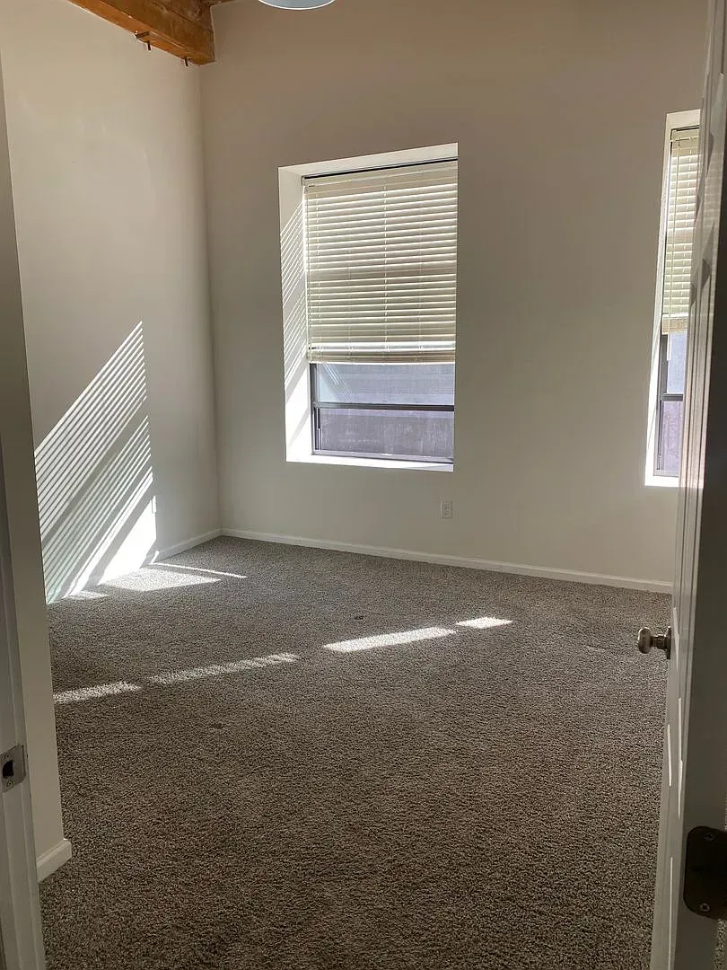 Empty room with neutral-colored carpet and blinds. Sunlight streams through the window.