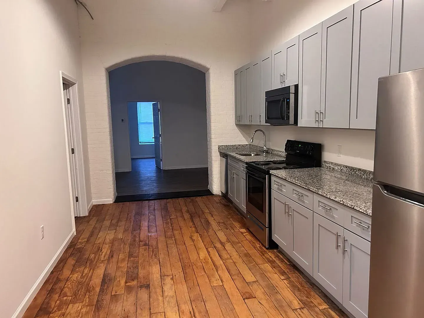 Kitchen with wood floor, gray cabinets, stainless steel appliances, and an arched doorway.