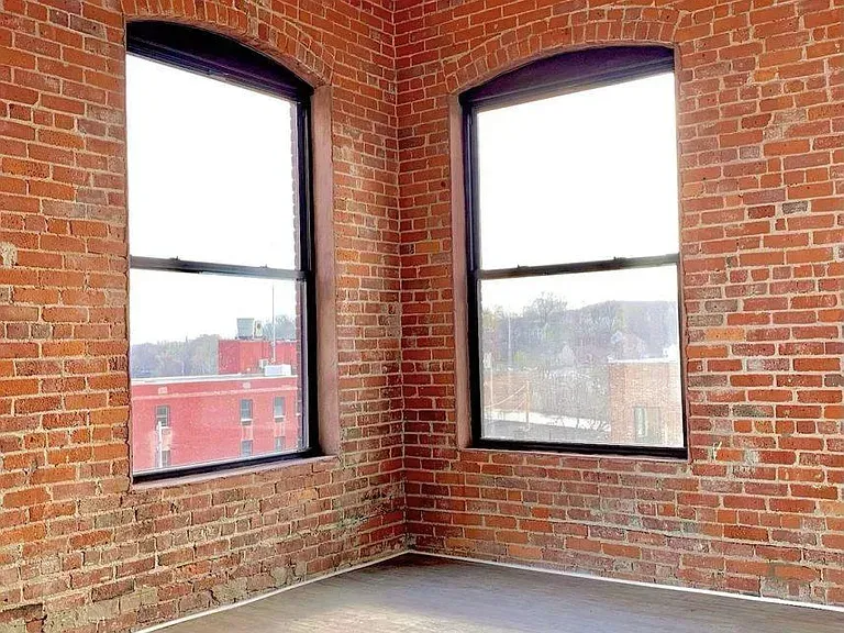 Two arched windows in a brick-walled room. Sunlight streams in. City buildings visible outside.