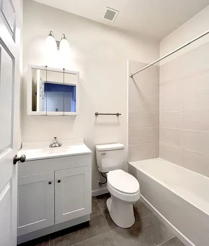White bathroom with vanity, toilet, and bathtub. Gray tiled floor and walls.