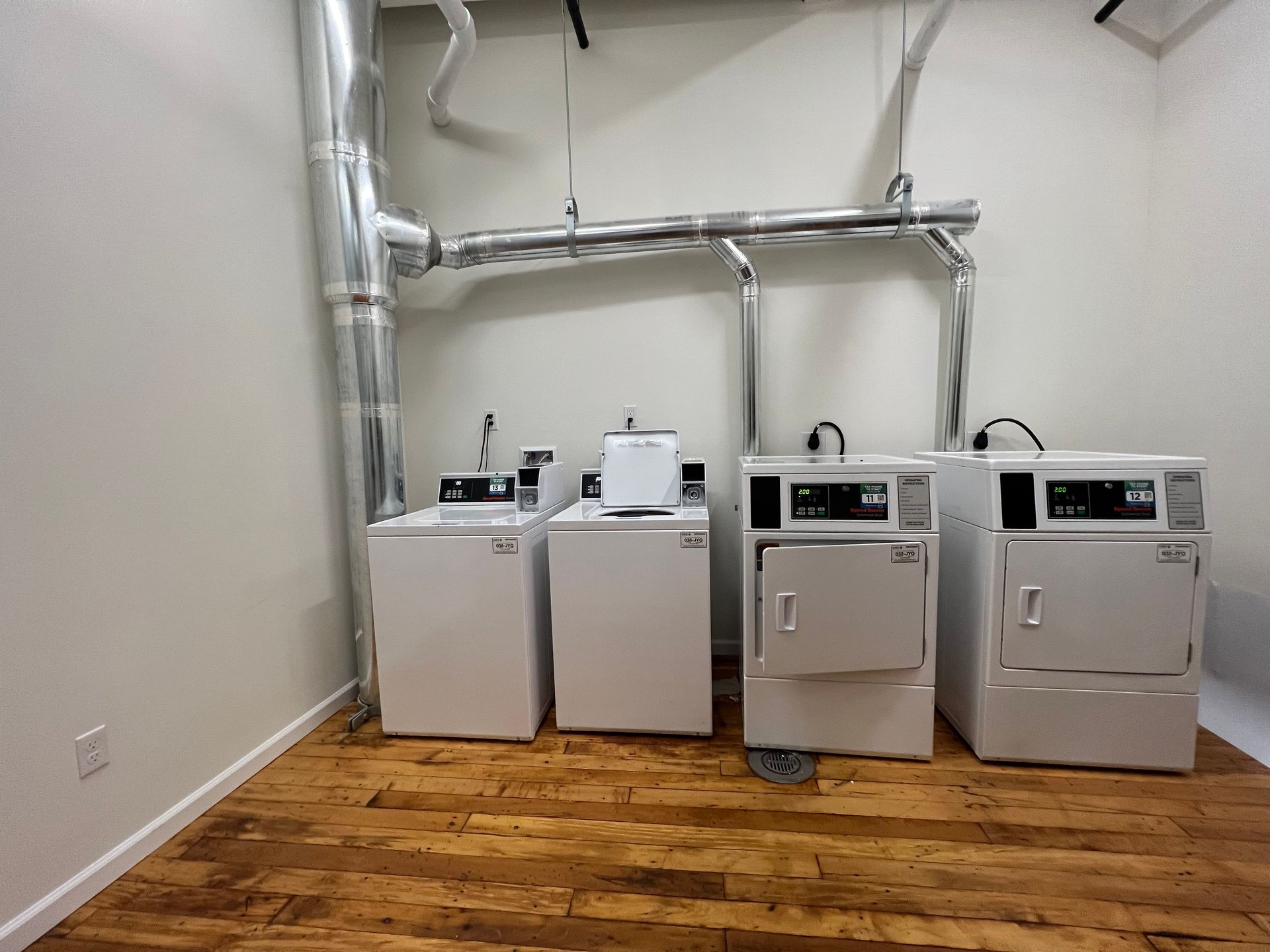 Laundry room with two washers, two dryers, and a utility sink. Silver pipes run above the machines.
