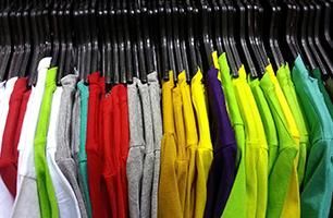 Filas de camisetas coloridas colgadas en perchas negras.