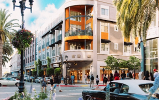 Street scene with pedestrians, cars, and buildings with shops. Palm trees and a multi-story building with orange accents.