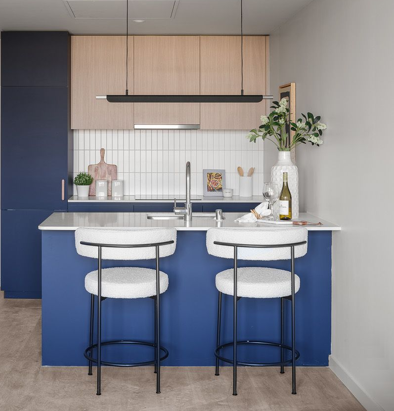 Modern kitchen with blue island, wooden cabinets, and white bar stools.