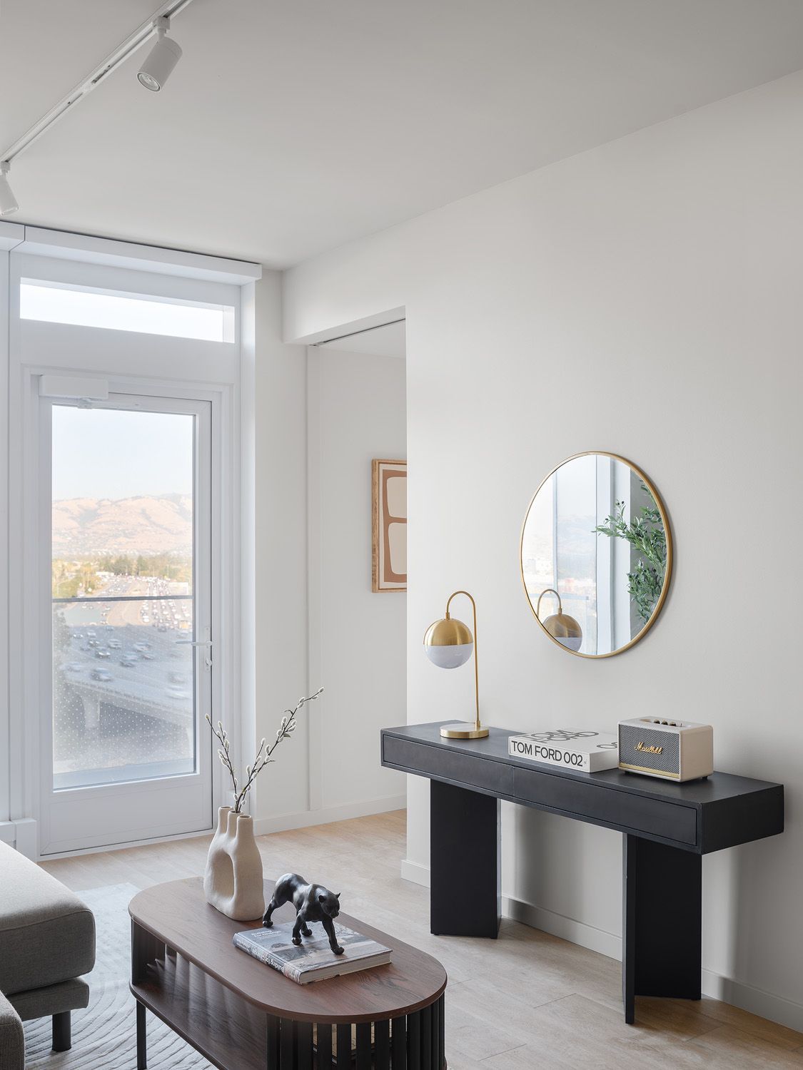 Living room with modern decor, a black console table with mirror and lamp, and a view of mountains.