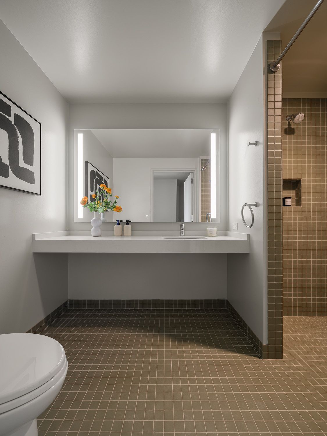 Bathroom with vanity, toilet, and shower. Gray and brown tones. Rectangular mirror with lights.