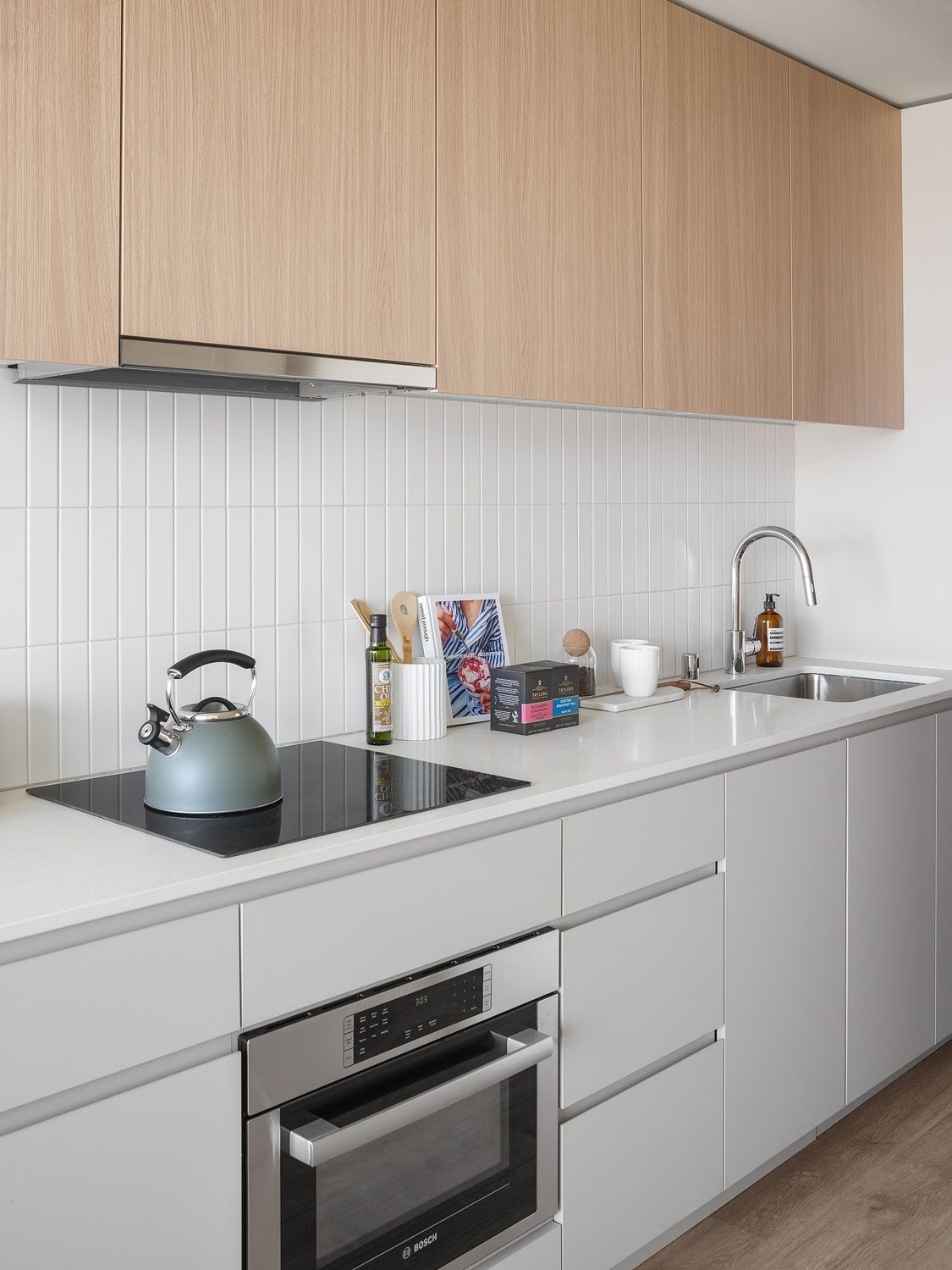 Modern kitchen with light wood upper cabinets, gray lower cabinets, and a white countertop.