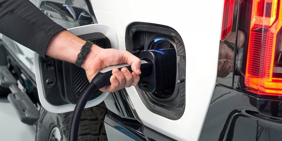 A hand plugging a charger into an electric vehicle.