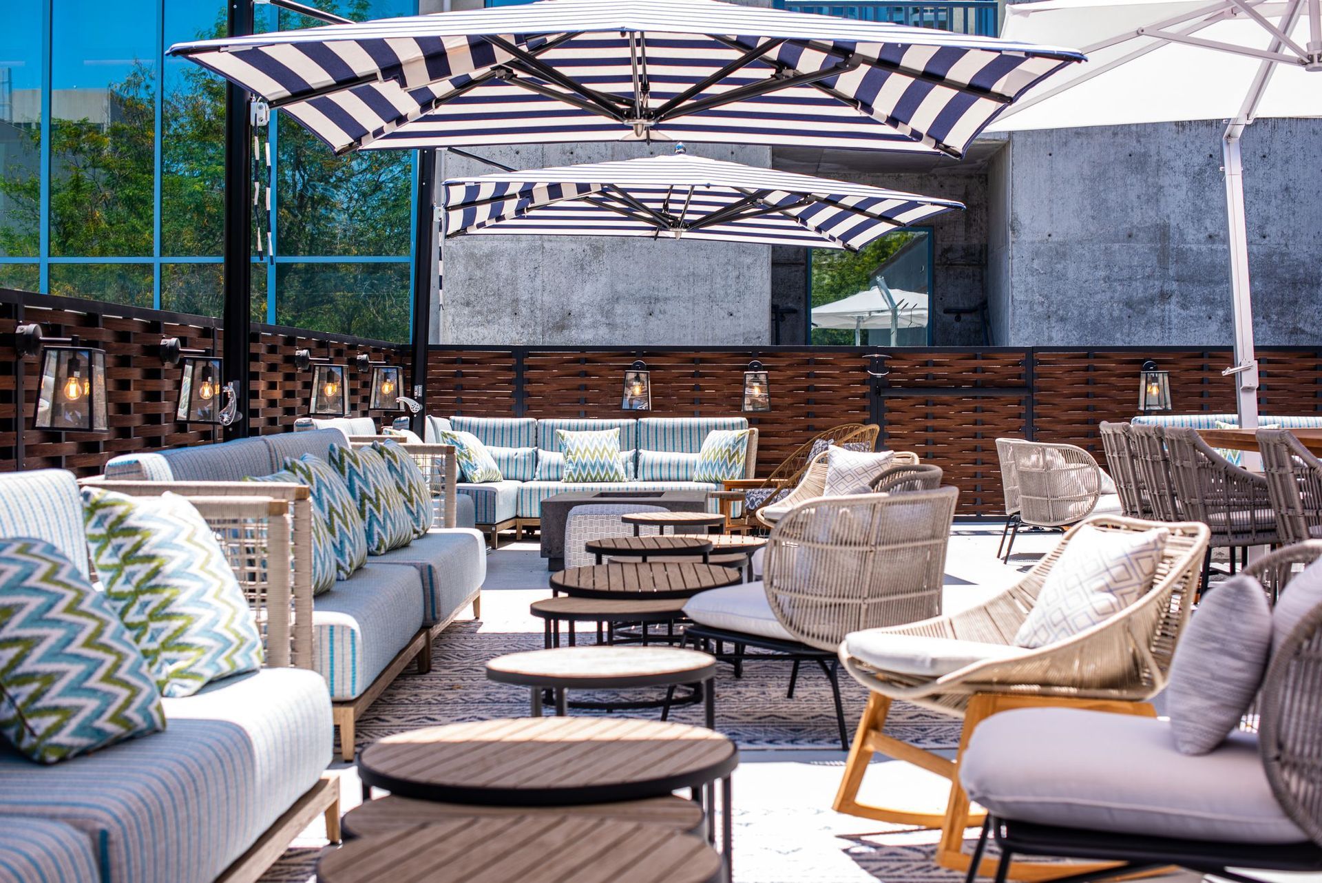 Rooftop patio with striped umbrellas, couches, chairs, and small round tables; sunny day.