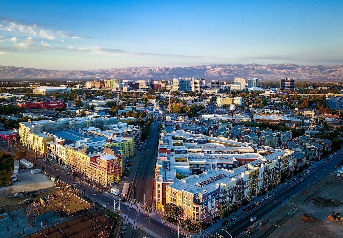 Aerial view of a city with buildings, roads, and mountains in the background under a blue sky.