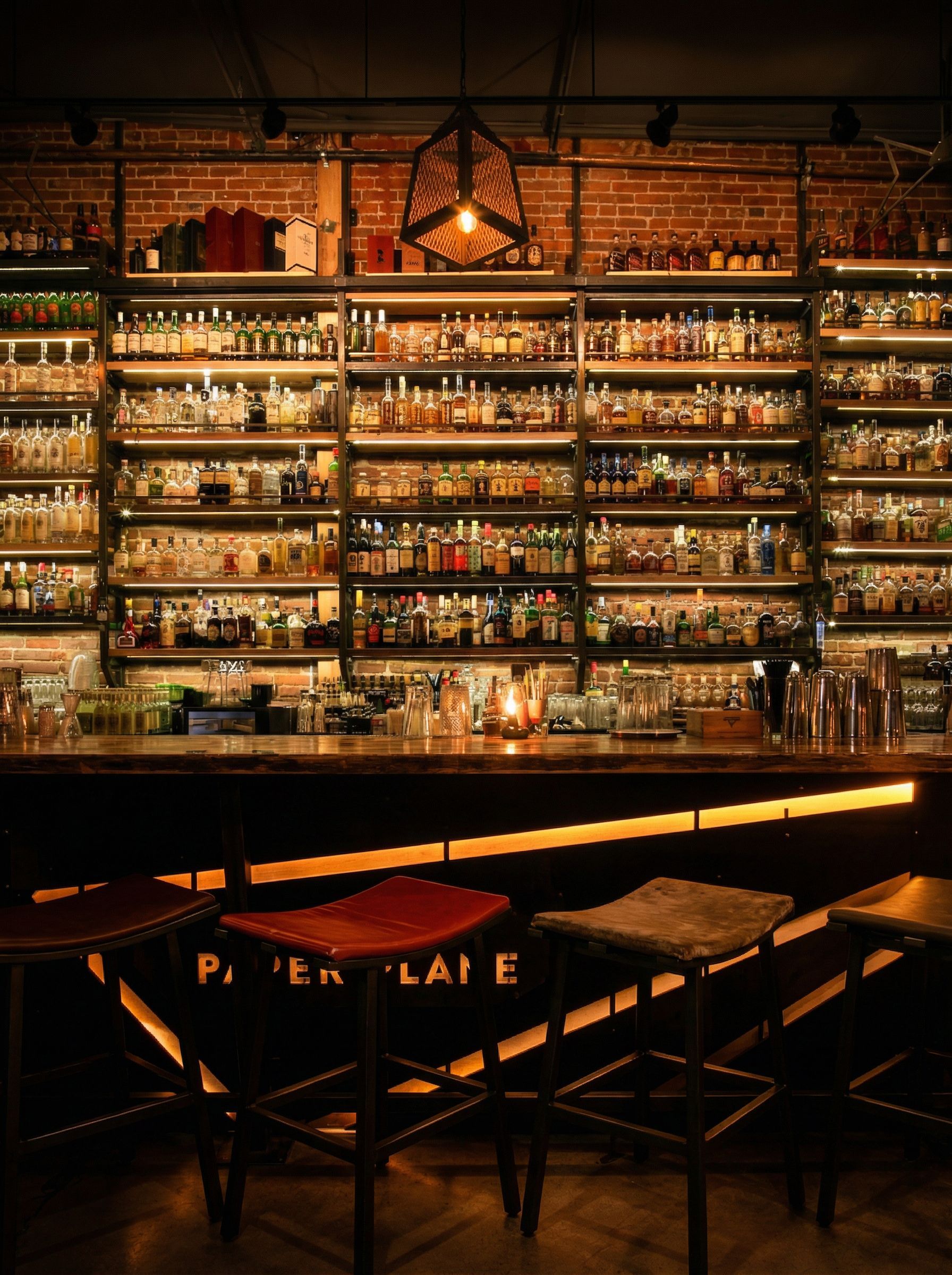 Bar interior with lit shelves of liquor bottles and stools at the counter.