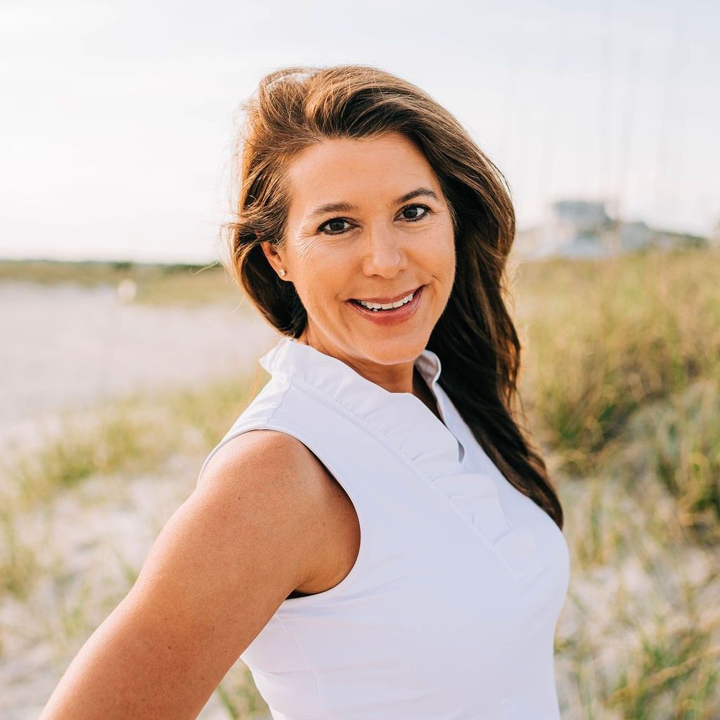 A woman in a white shirt is standing in a field and smiling.