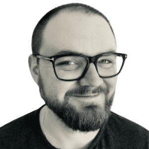 En man med skägg och glasögon ler på ett svartvitt foto.