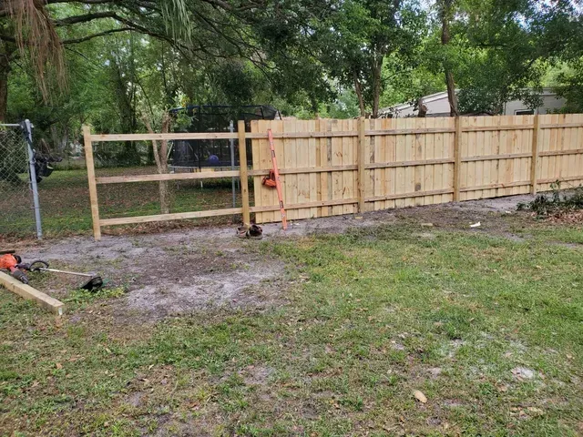 New wooden fence being built in a yard with grass and trees in the background.