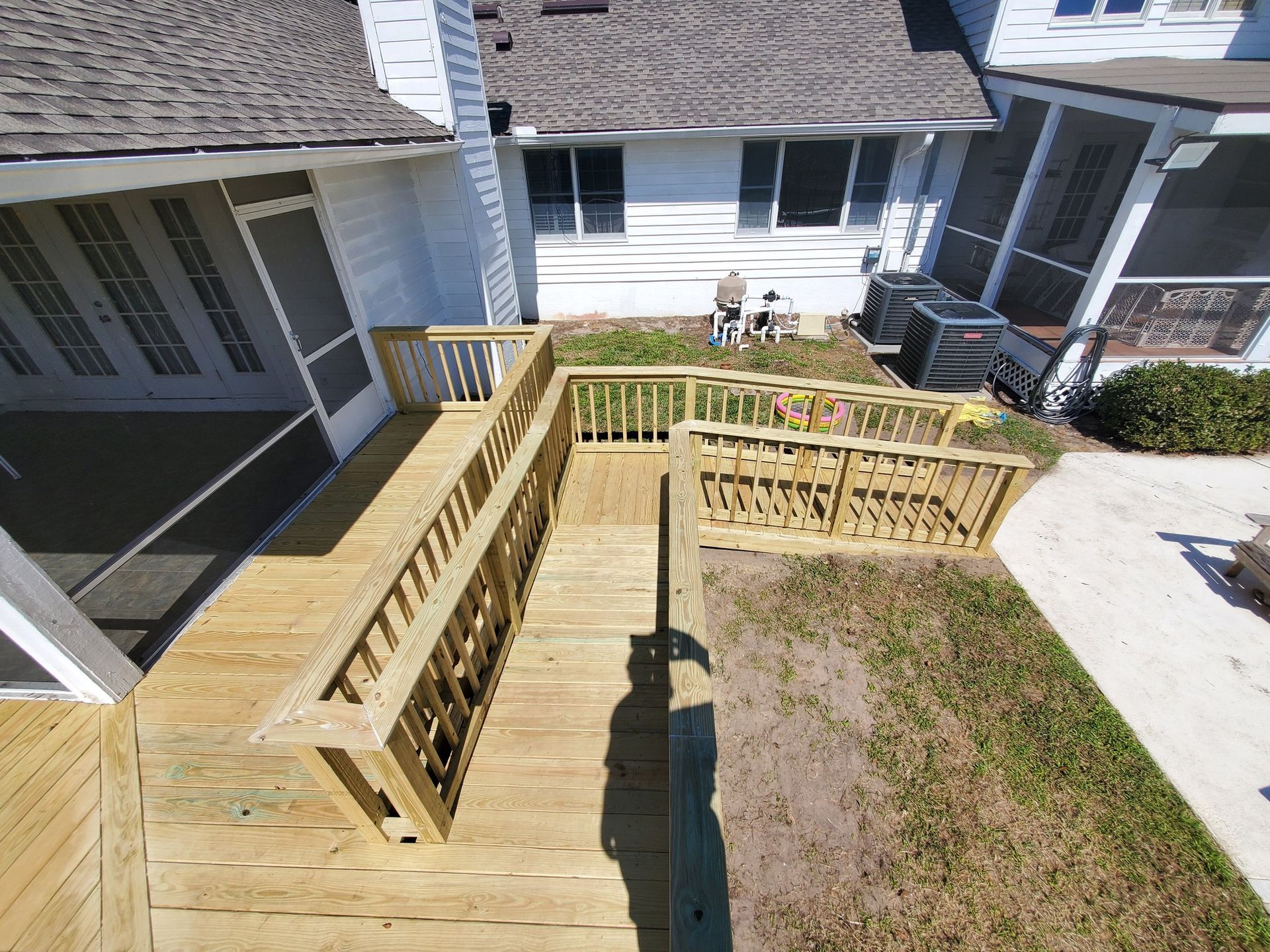 Wooden ramp and deck providing accessible entry to a white house with screen porches; sunny day.