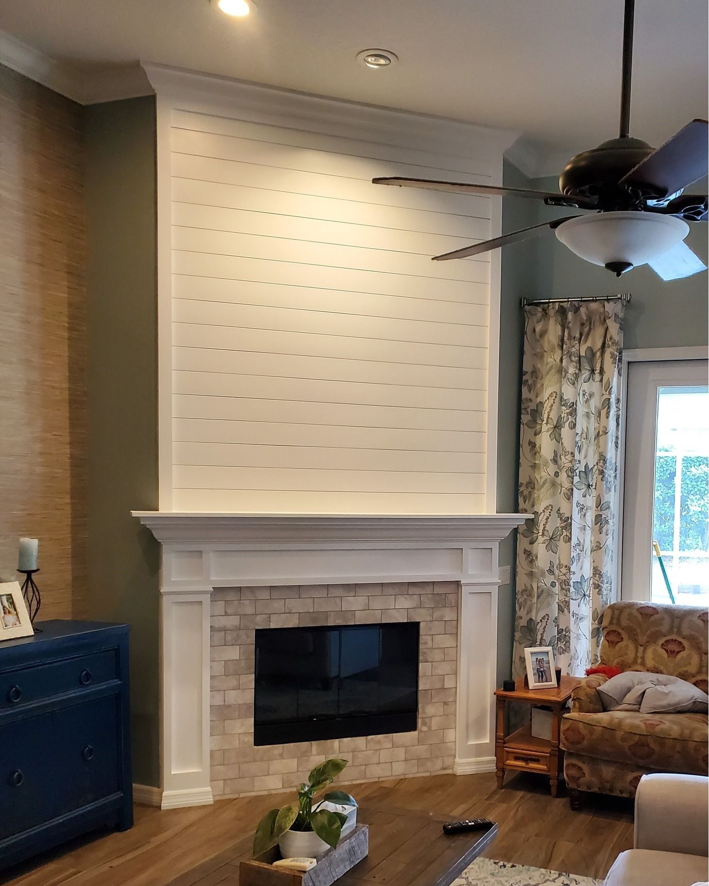Fireplace with white mantle and brick surround, against a white shiplap wall.  A blue cabinet is on the left.