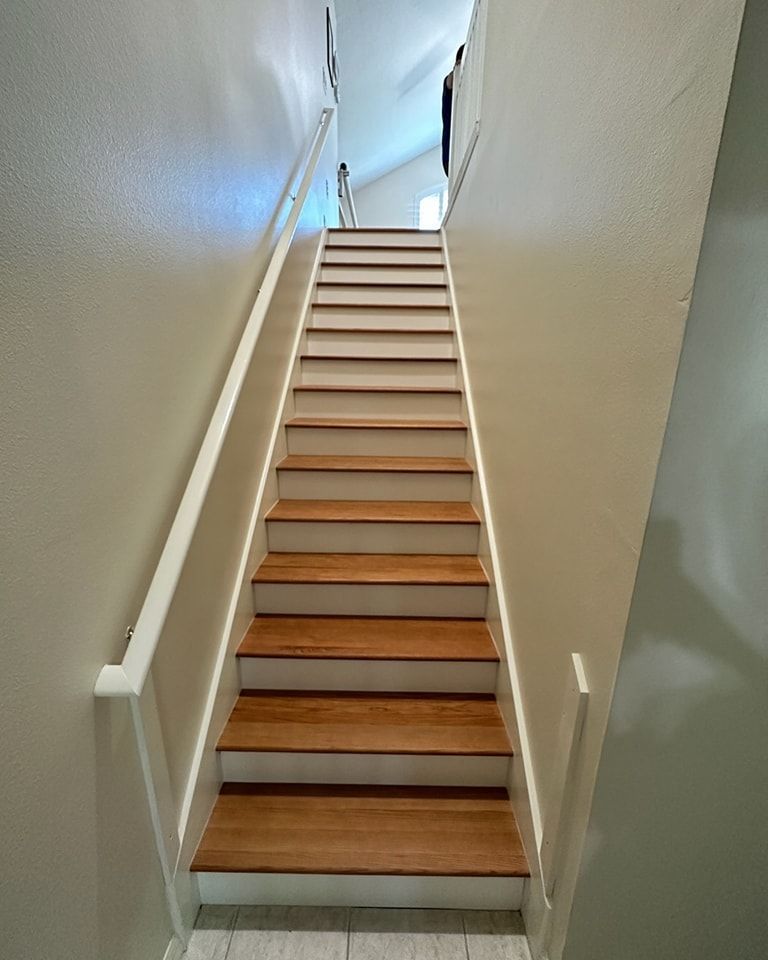 Wooden staircase with white risers and handrails, beige walls.