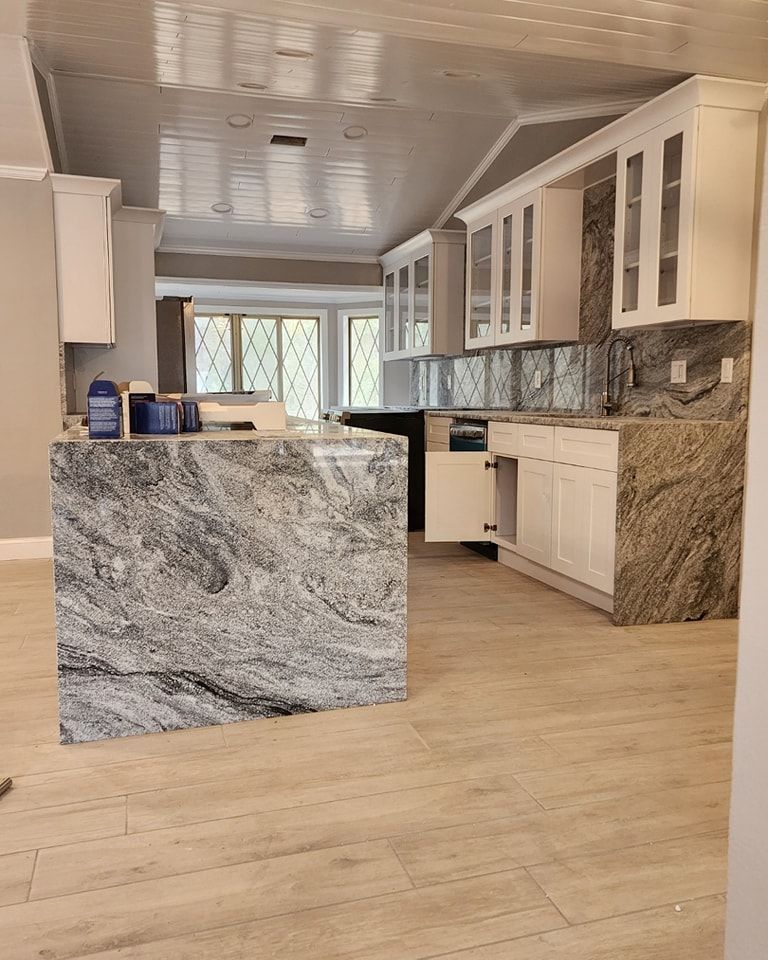 Newly renovated kitchen with granite countertops, white cabinets, and island. Light wood floors and a reflective ceiling.