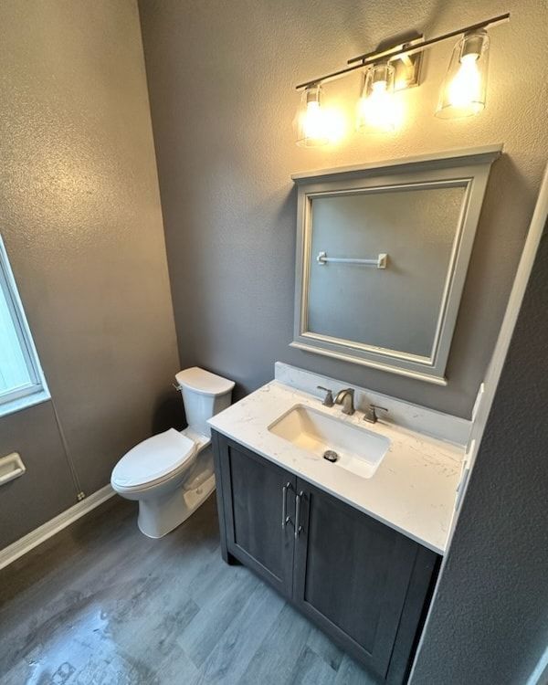 Bathroom with gray walls, vanity, toilet, and lit vanity lights.