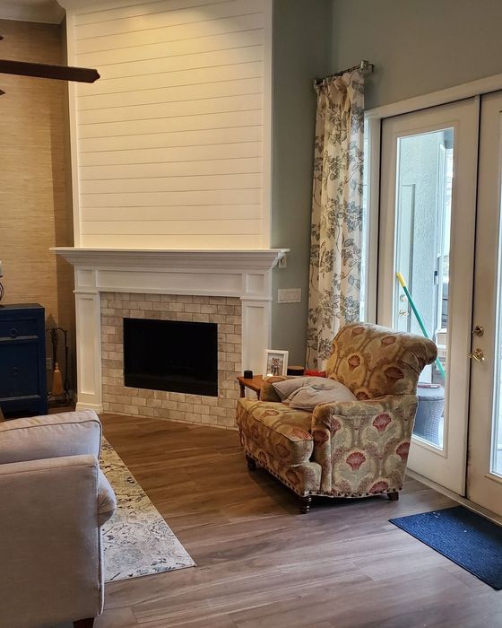 Living room with fireplace, chair, and doors. Fireplace has stone base, white mantel, and wood wall.
