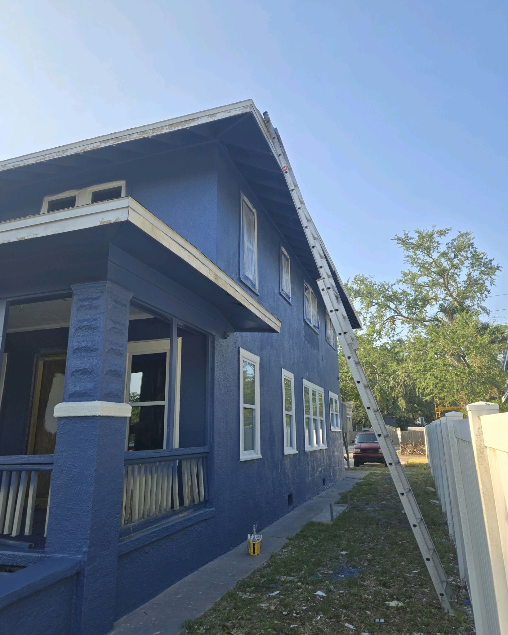Blue house with white trim, ladder against the side, clear sky.