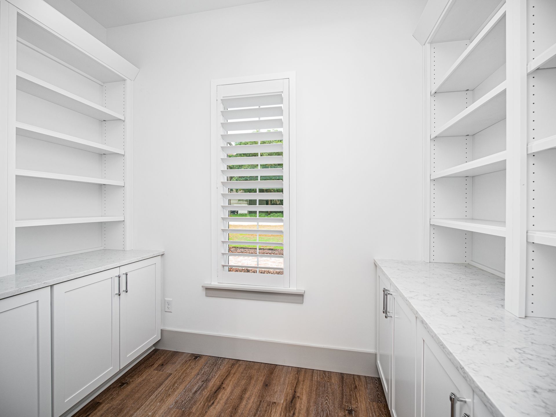 White built-in shelving and cabinets with a window, in a room with wood flooring.