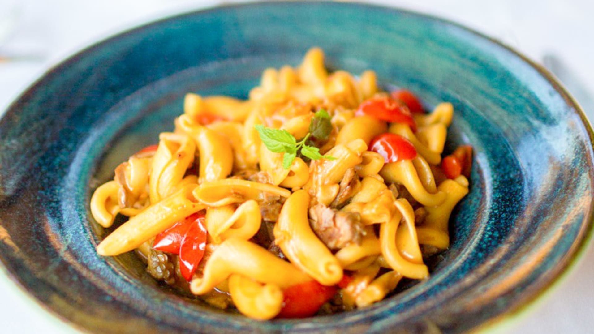 Un primo piano di una ciotola di pasta con carne e pomodori su un tavolo.