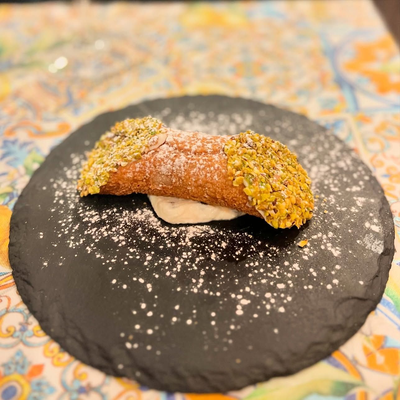 Primo piano di un cannolo su un piatto nero su un tavolo.