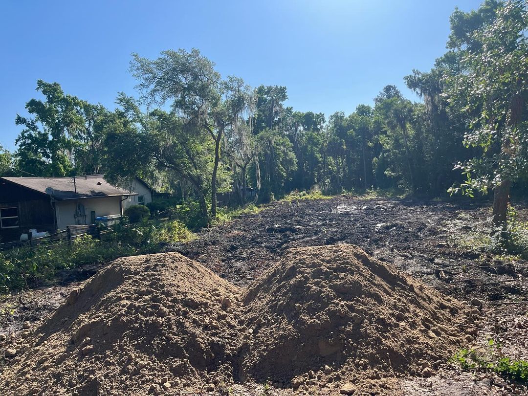 A pile of dirt is sitting in front of a house surrounded by trees.
