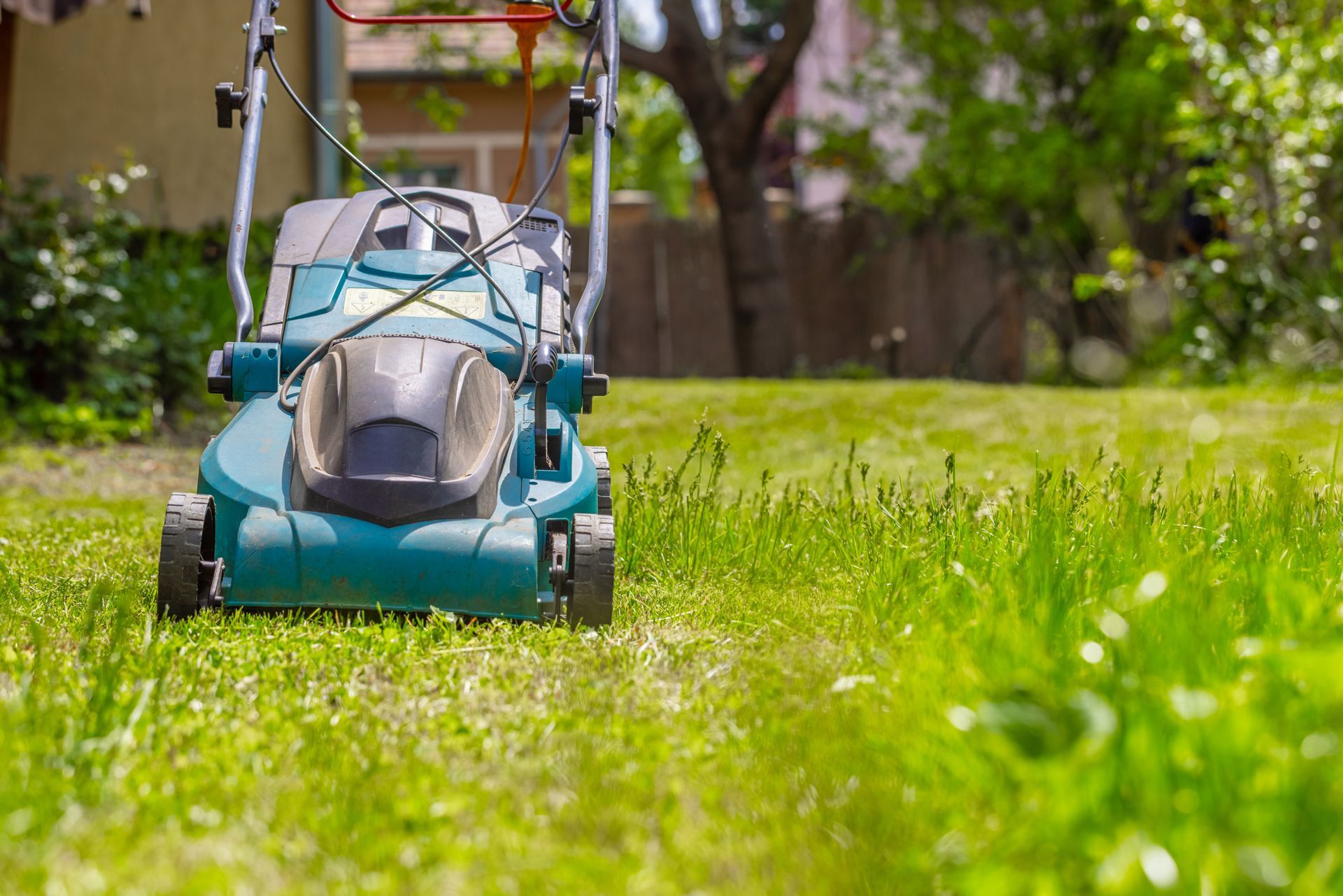 A lawn mower is cutting a lush green lawn in a backyard.