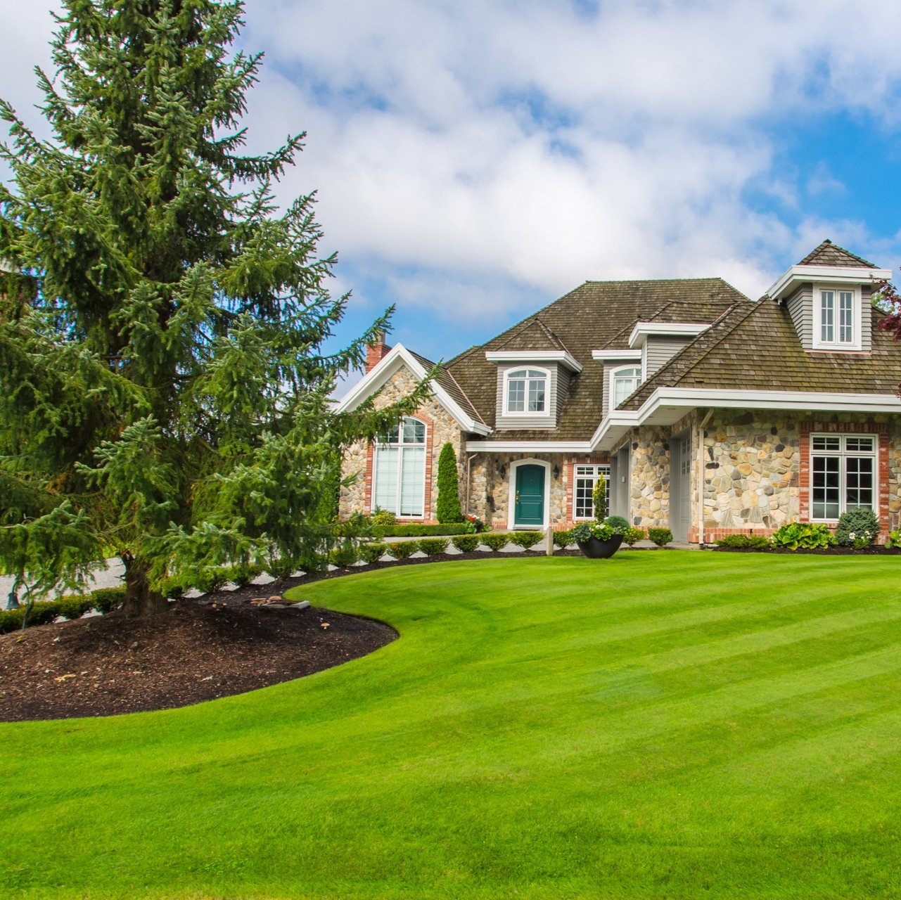 Stone house with green lawn and landscaping under a blue sky.