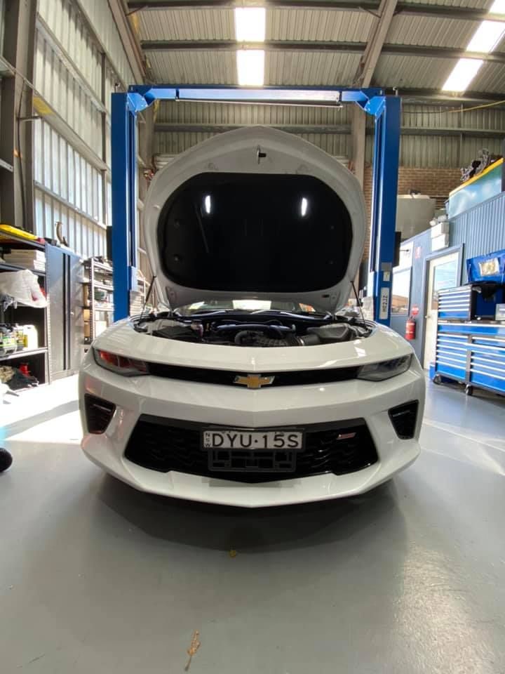 White Chevrolet Camaro with hood open in a garage, under a blue lift — D.A.G Automotive in Unanderra, NSW