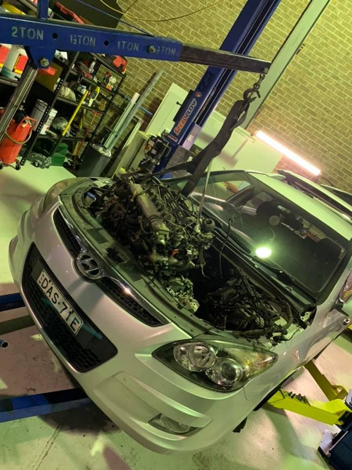 A car engine being lifted out of a silver Mazda in a garage using a crane. — D.A.G Automotive in Unanderra, NSW
