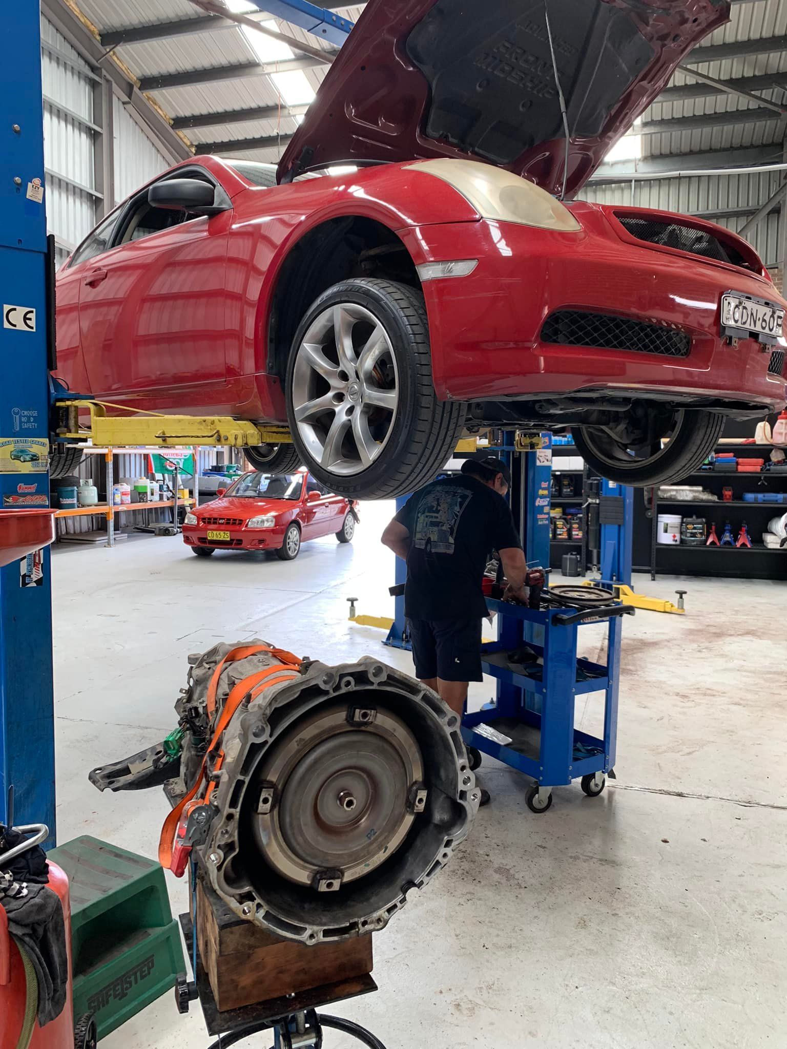 Red Car on a Lift in a Garage, a Mechanic Working — D.A.G Automotive in Unanderra, NSW