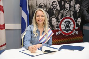 A woman is sitting at a table in front of a flag.