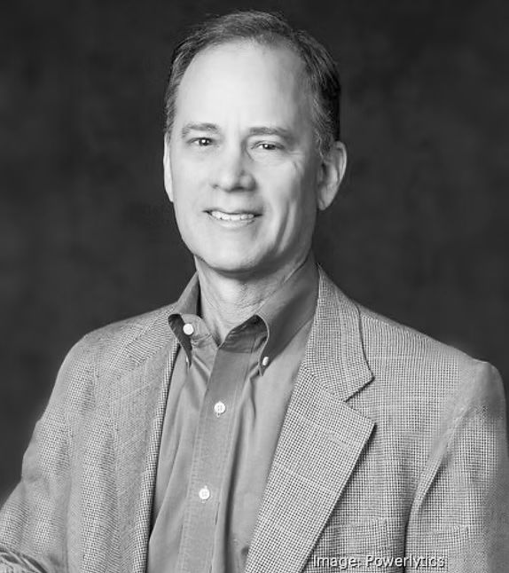 Man with light skin smiling, wearing a button-down shirt and a blazer, posing for a headshot.