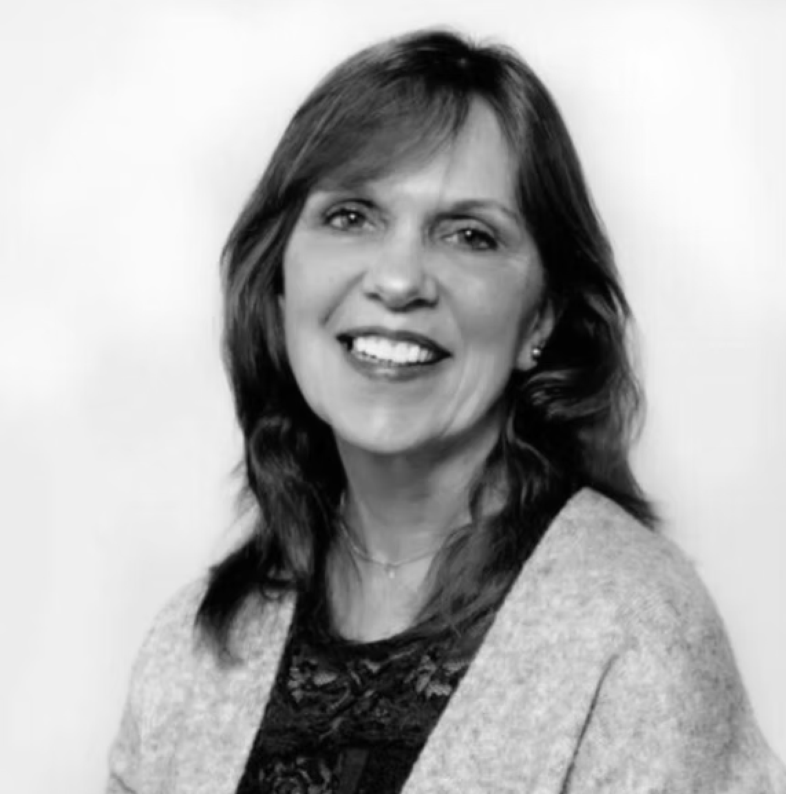 Woman with shoulder-length brown hair smiling, wearing a black lace top and light gray cardigan.