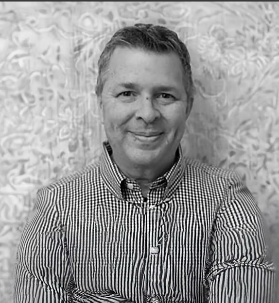 Man in striped shirt smiling, standing in front of a patterned background.