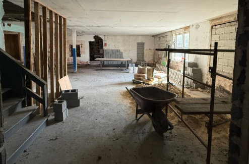 Interior of a building under renovation with construction materials, a wheelbarrow, and exposed walls.