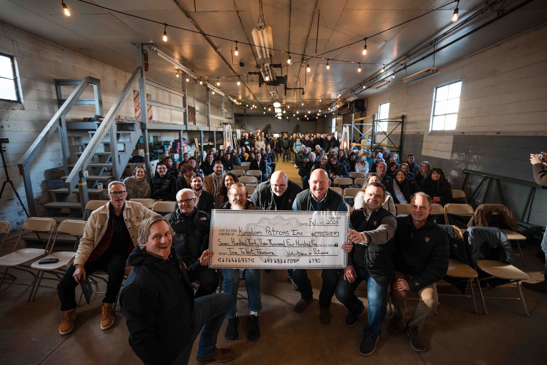 Group of people holding a sign in a large indoor space, with many others seated; string lights above.