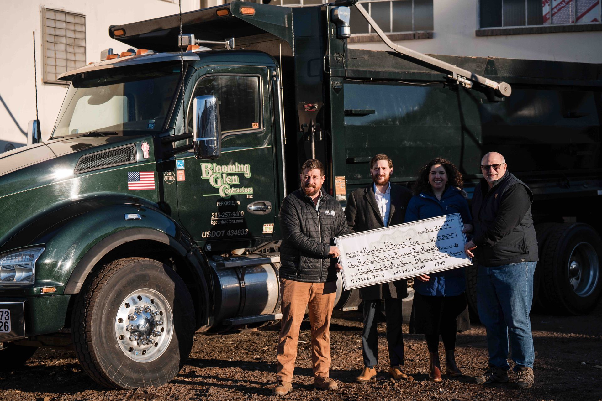 Four people pose with a giant key in front of a dark green dump truck.