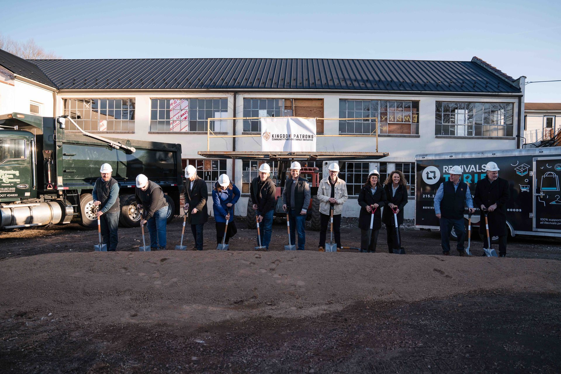 People with shovels stand in front of a building, ground breaking ceremony.