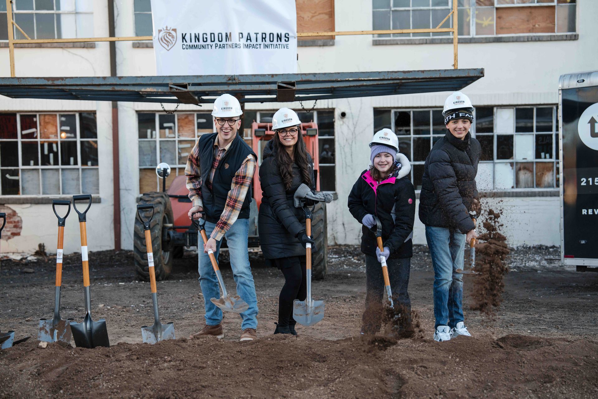 People with shovels at a groundbreaking event in front of a building; dirt and construction equipment visible.