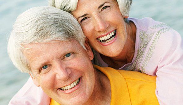 senior couple on the beach smiling with beautiful white teeth