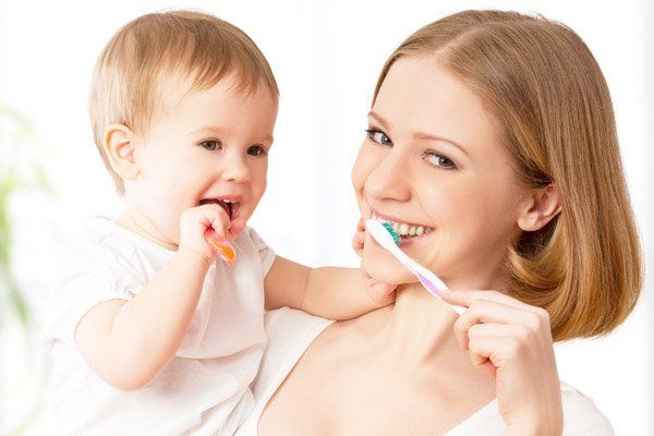 mother showing how to brush teeth to baby