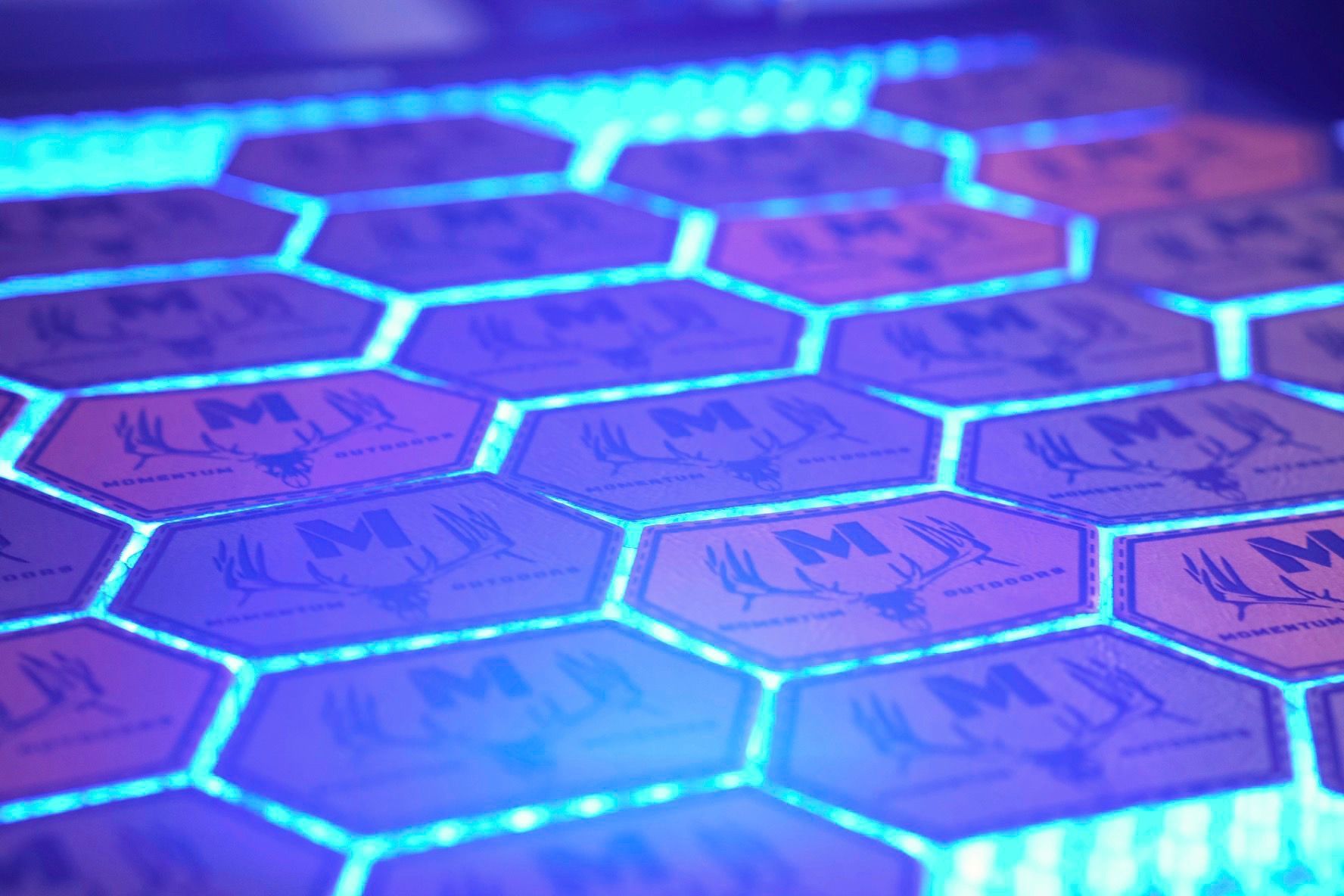 A bunch of leather hat patches are glowing in the dark under a blue light.