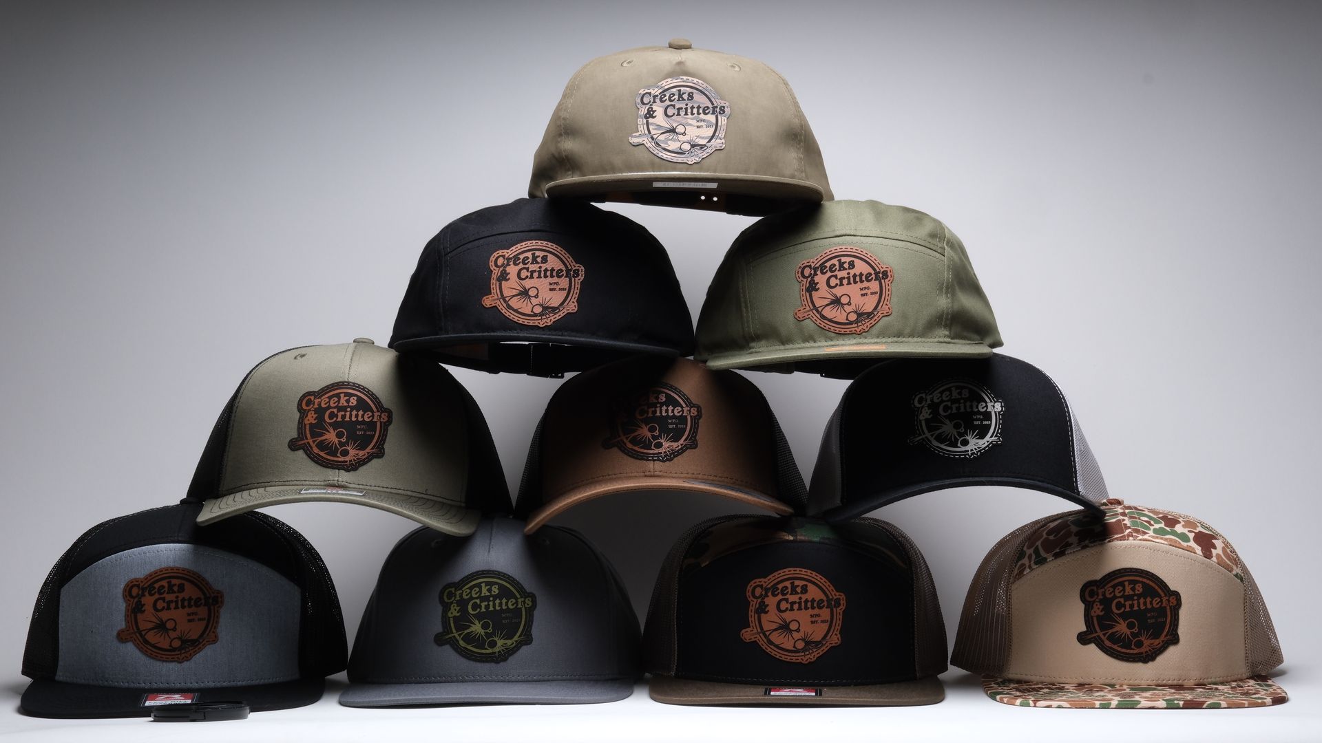 A pyramid arrangement of ten baseball caps in various colors, each featuring a centered circular logo patch.