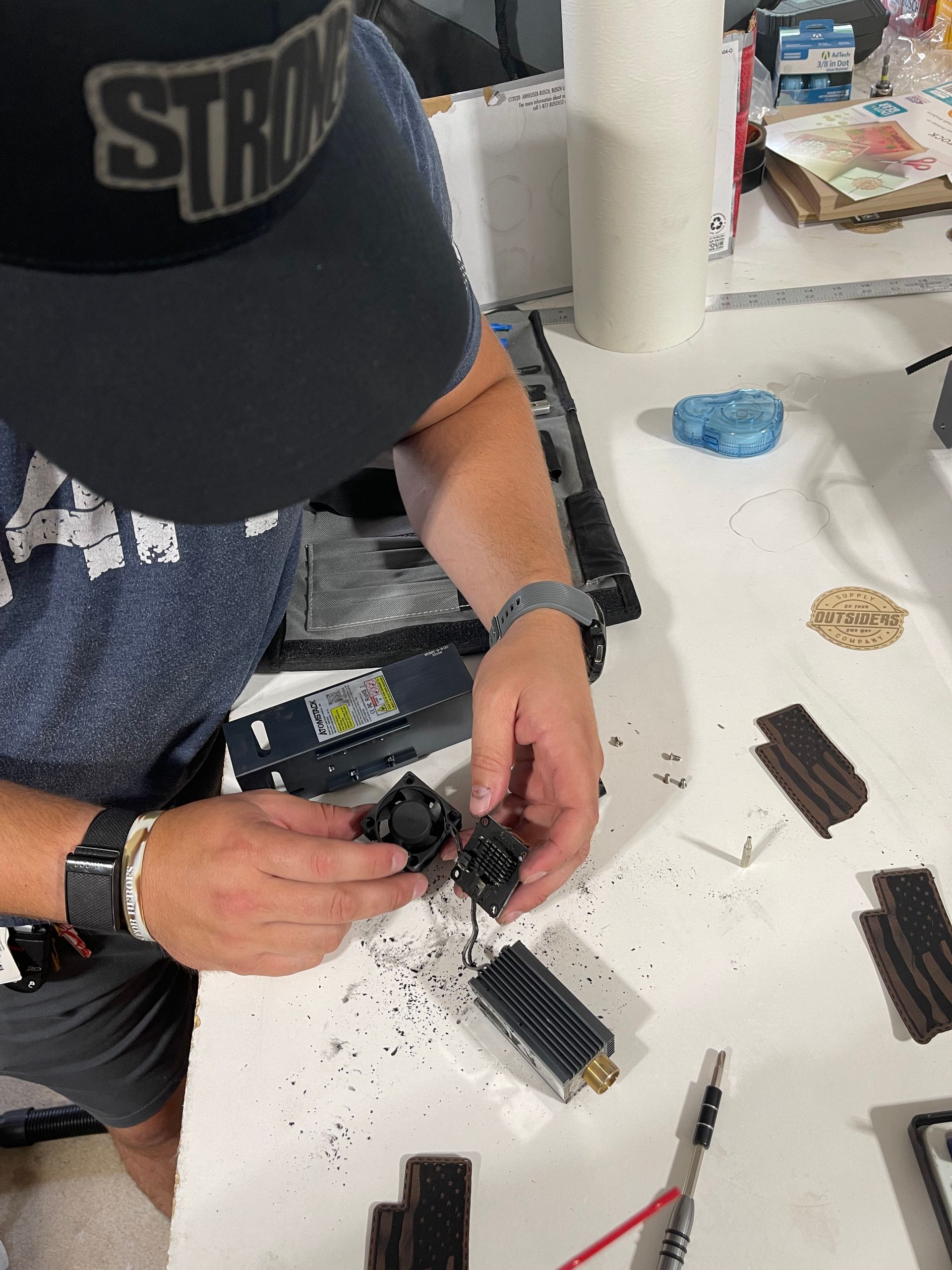 A man wearing a custom leather patch hat hat is working on a laser engraver