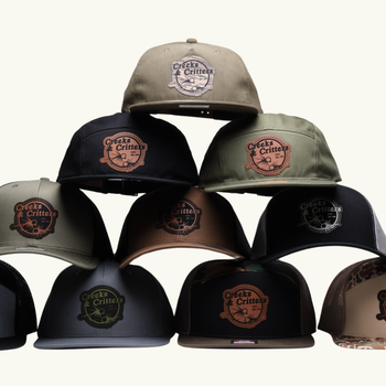 A bunch of hats with custom leather patches for a fly fishing business are stacked on top of each other on a white background.